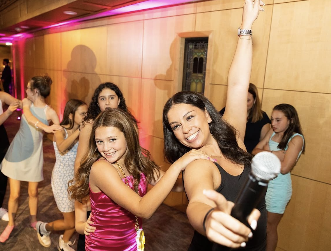 ILP MC celebrating with a Bat Mitzvah guest as friends dance in the background