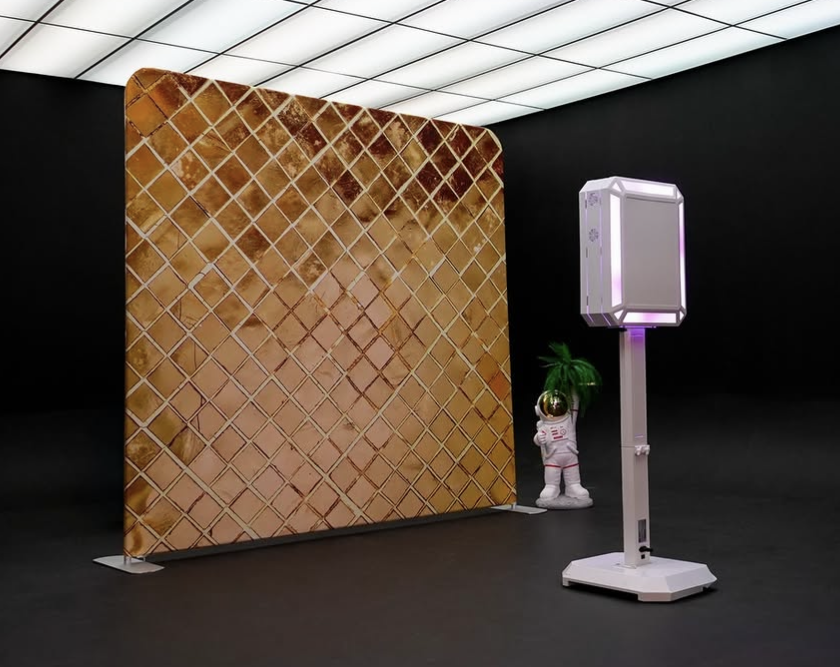 Gold sequined photo booth backdrop with a modern white kiosk and astronaut figure