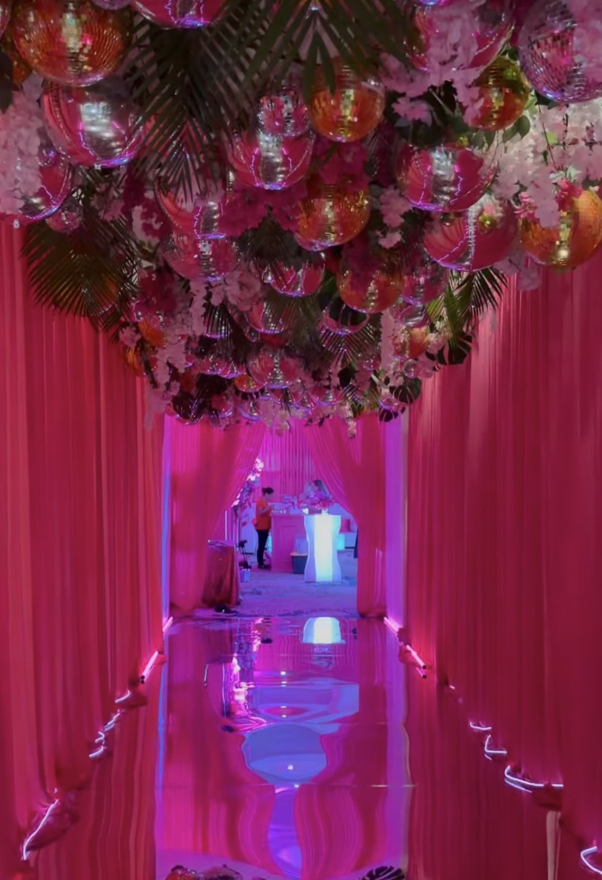 Vibrant tropical disco entrance with pink draping, disco balls, and palm greenery
