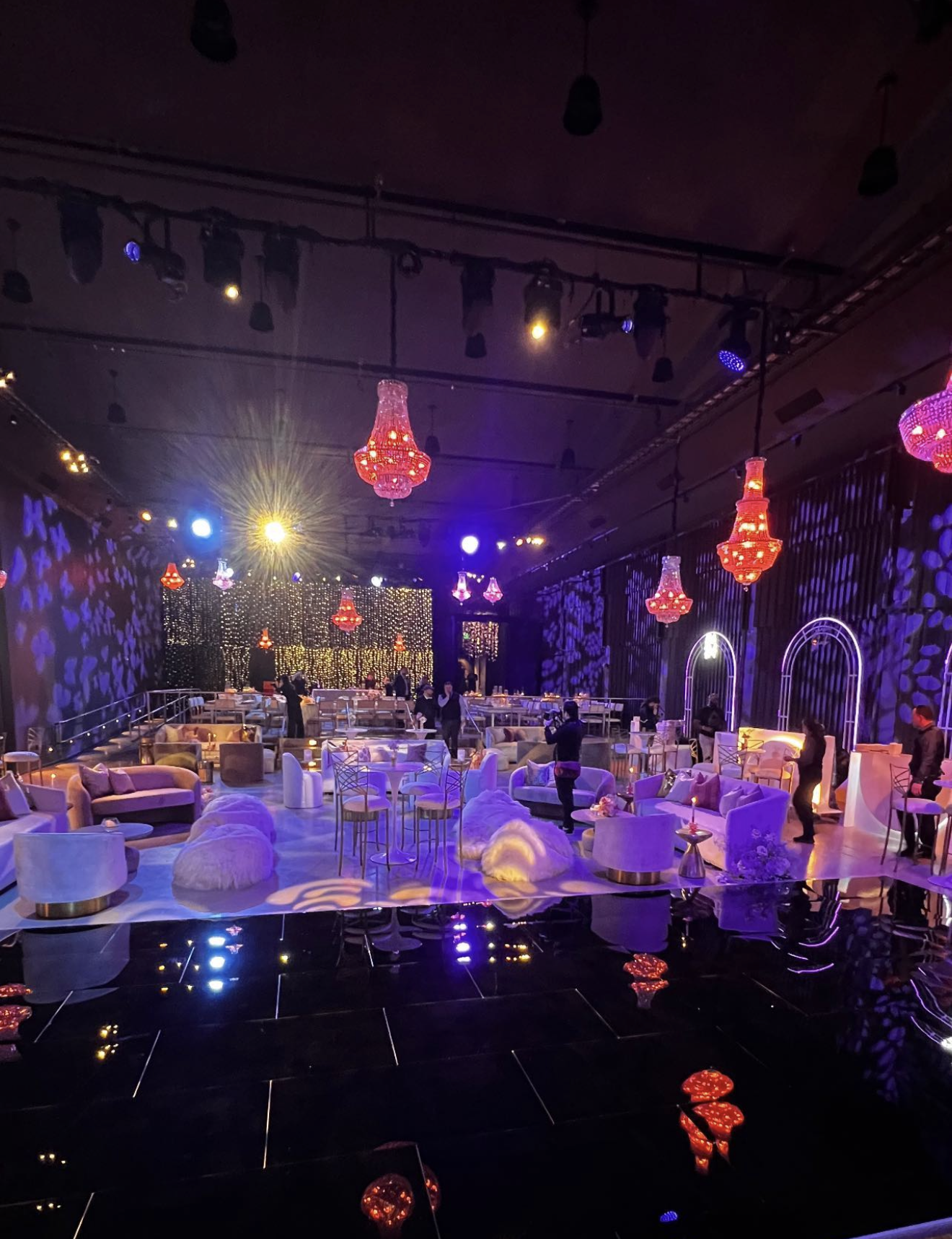 Luxury event lounge with purple and pink lighting, plush seating, and glowing chandeliers